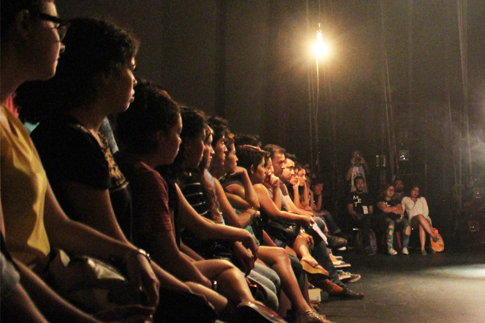 Foto de una audiencia de frente viendo una obra de teatro.